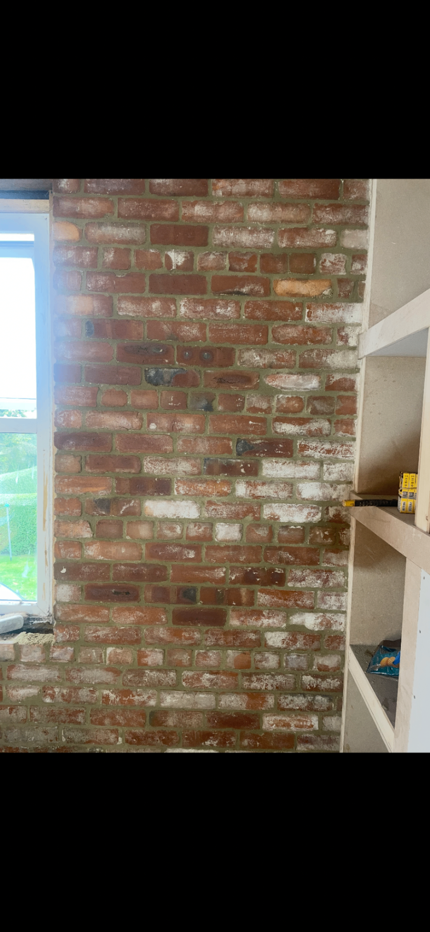 Interior exposed brick feature wall beside built-in shelving and a window.