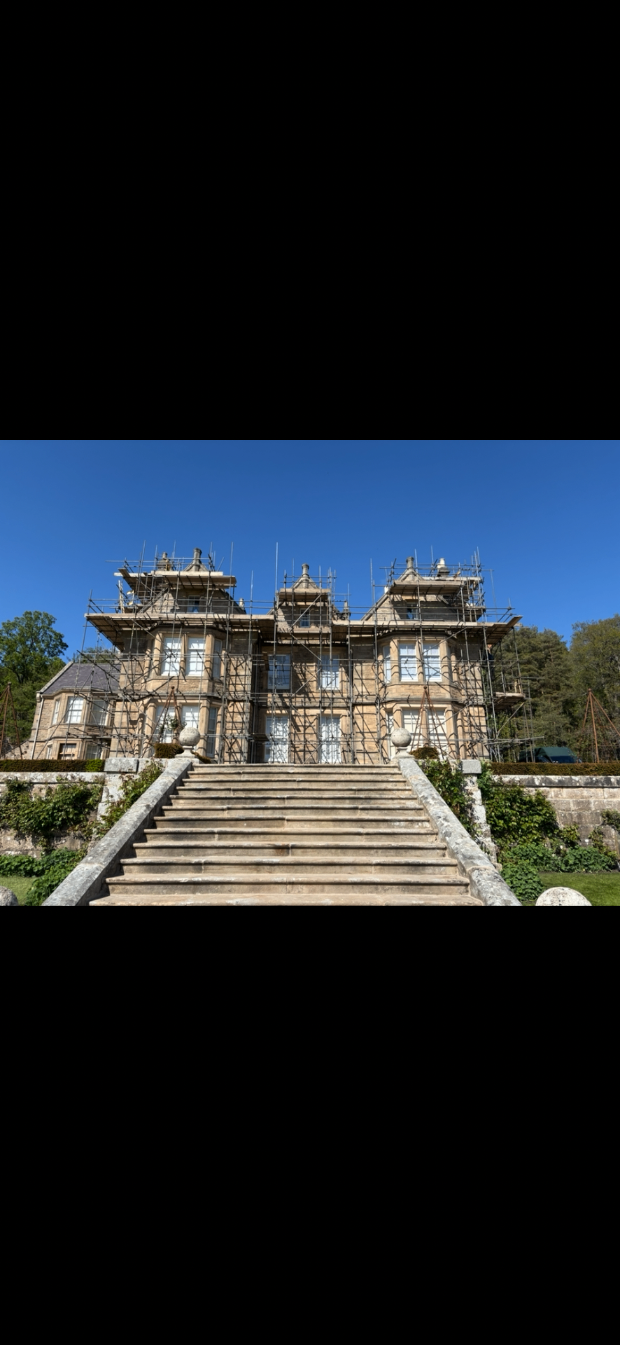Grand Victorian sandstone country manor under full external restoration with scaffolding to the front elevation, viewed from a formal stone staircase.