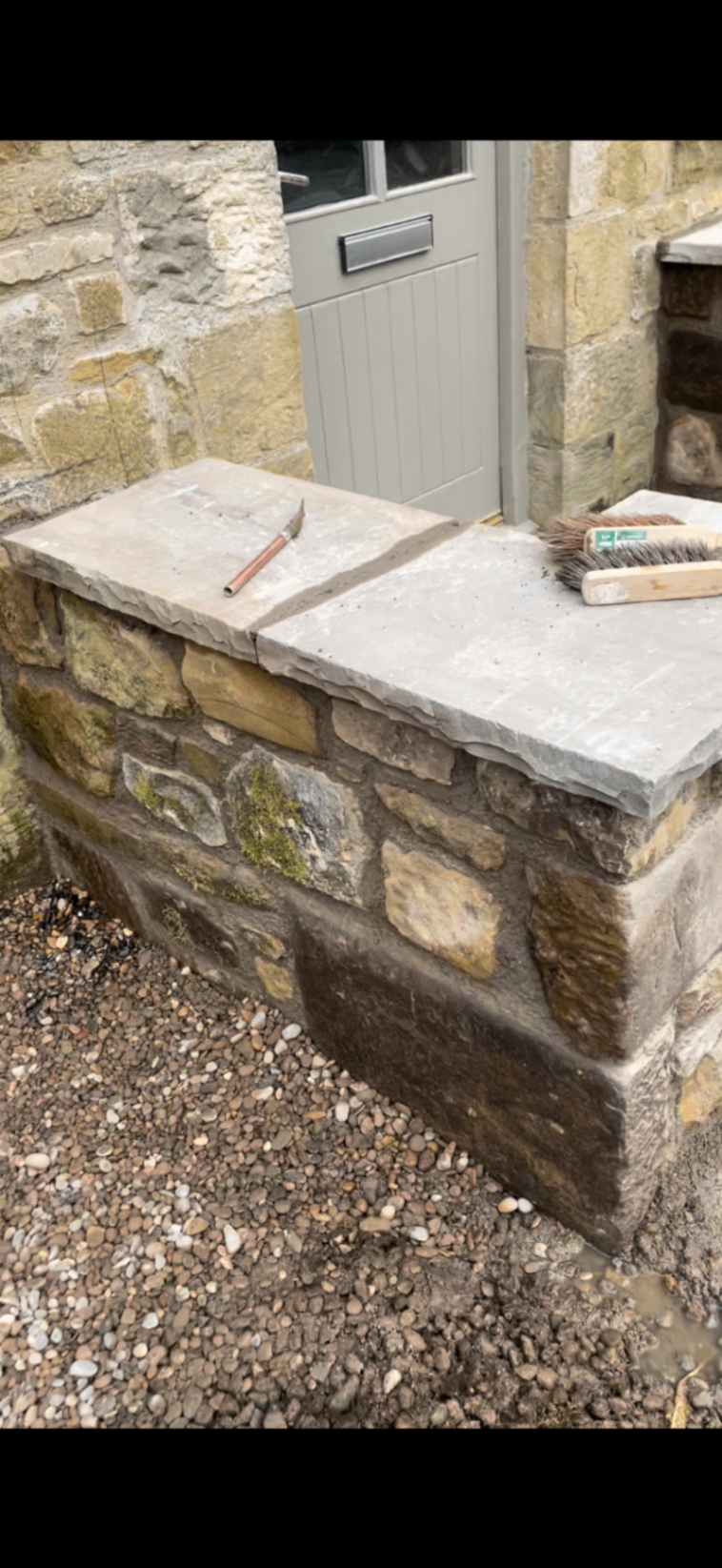 Close-up of finished natural stone walling with stone coping beside a doorway.