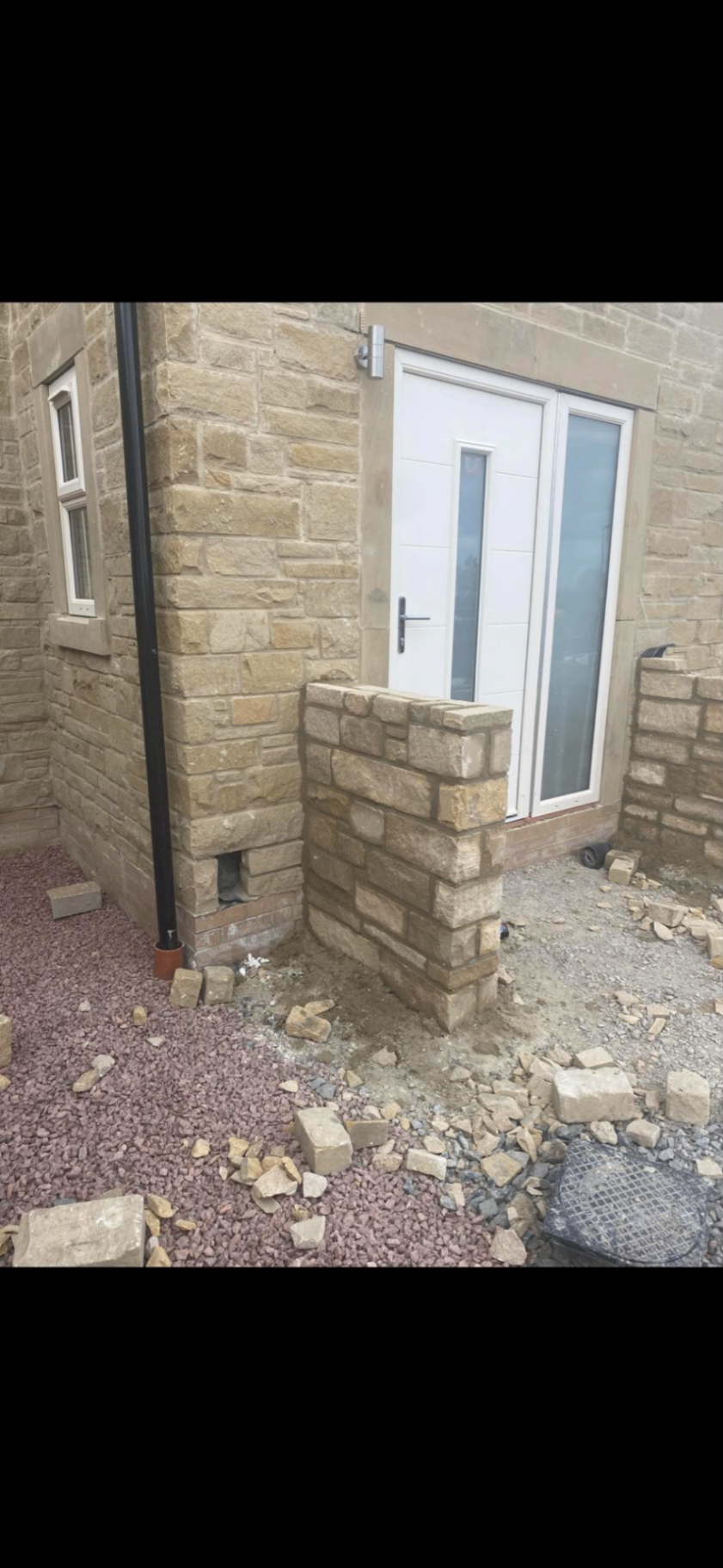Natural stone entrance wall and gate pier detail beside a modern white door.