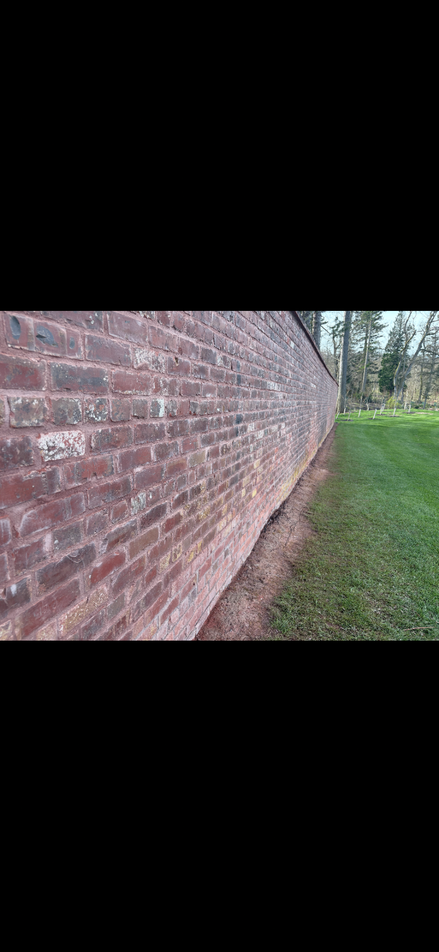 Long red brick boundary wall running alongside a lawned garden in Northumberland.