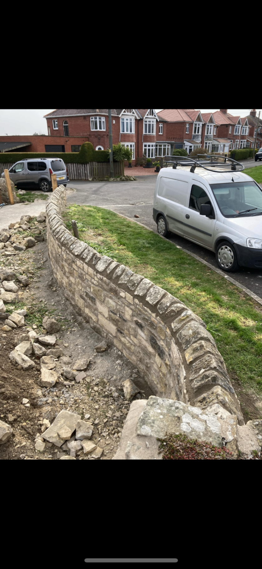 Curved natural stone roadside boundary wall completed along a front garden edge.