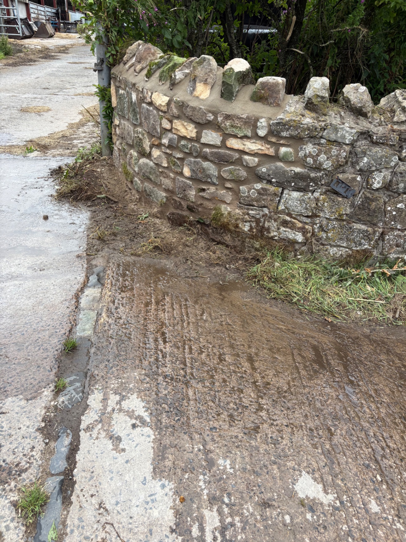 Curved roadside stone wall repair with fresh mortar and rebuilt coping stones.