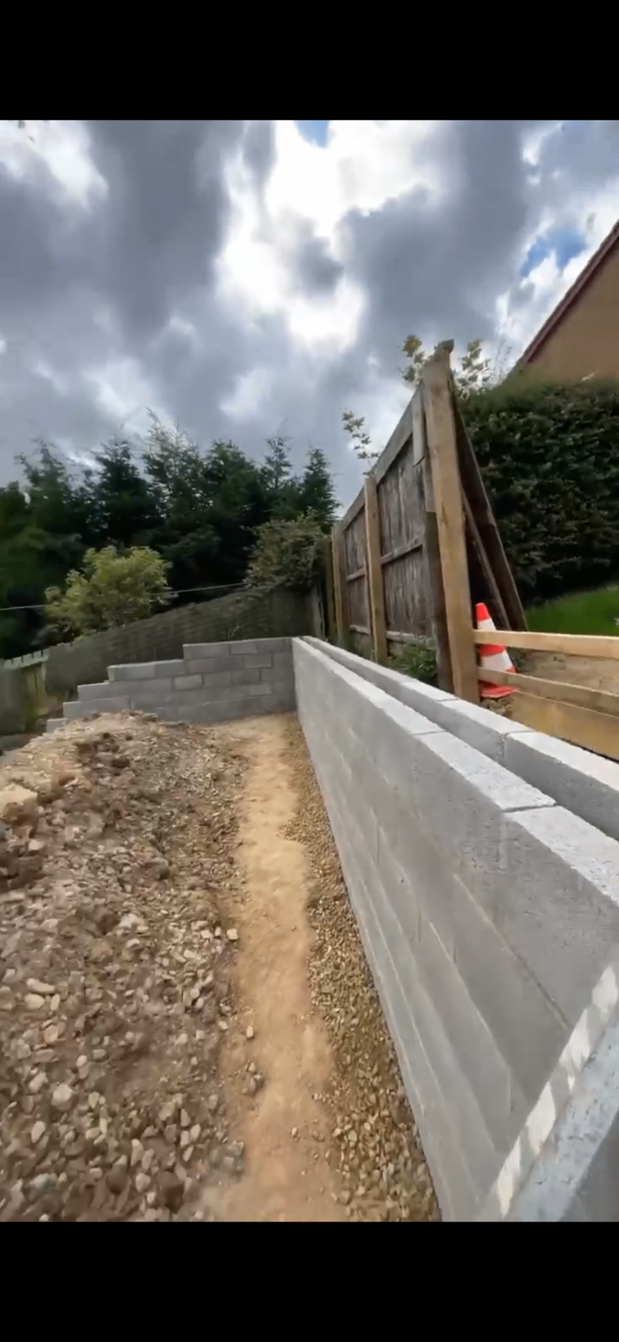 Concrete block retaining wall and stepped garden wall under construction beside existing fencing.